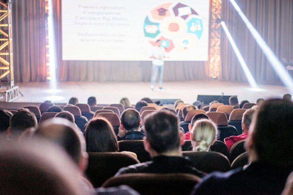 An insurance agent presenting information about Medicare to an engaged audience of seniors at a local seminar, with a projector screen showing key points.
